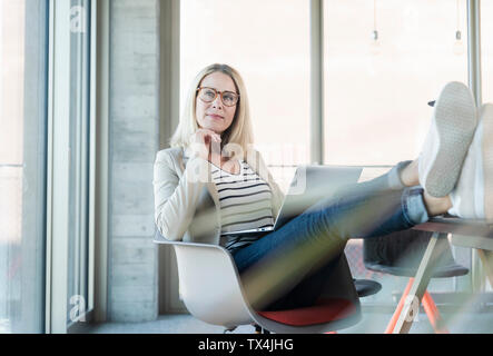 Ambiance businesswoman using laptop in office avec pieds Banque D'Images