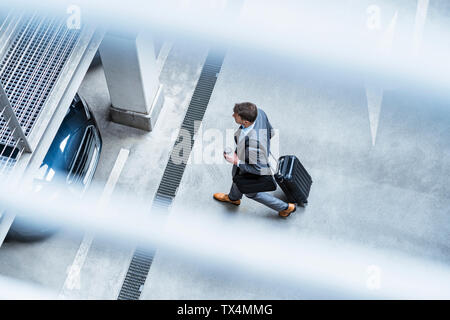 Vue de dessus du businessman walking avec café à emporter et des bagages dans un parking Banque D'Images
