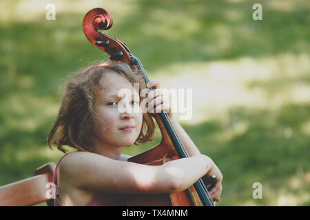 Une fille à jouer du violoncelle en jardin, à la recherche d'appareil photo Banque D'Images