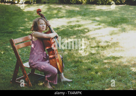 Une fille à jouer du violoncelle en jardin, à la recherche d'appareil photo Banque D'Images