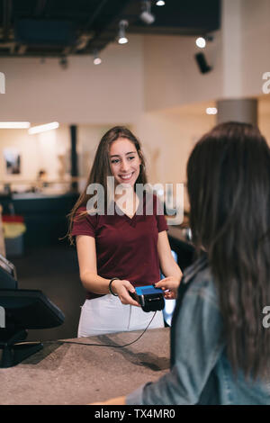 Jeune femme de payer sans espèces avec votre carte de crédit au guichet d'un café Banque D'Images