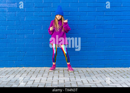 Girl wearing bouchon bleu et rose pull oversized standing in front of blue wall dancing Banque D'Images