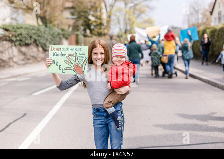 Fille avec bébé sur son bras tenant une plaque sur une démonstration de l'écologisme Banque D'Images