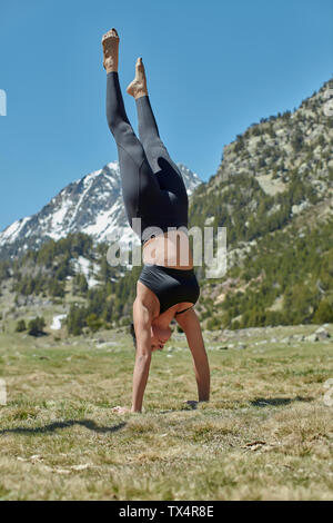 Young woman doing yoga dans la nature, handstand on meadow Banque D'Images