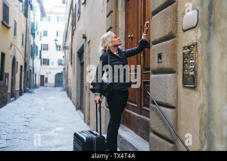 Italie, Florence, mature femme vêtue de noir se tenait devant la porte d'entrée avec rolling suitcase Banque D'Images