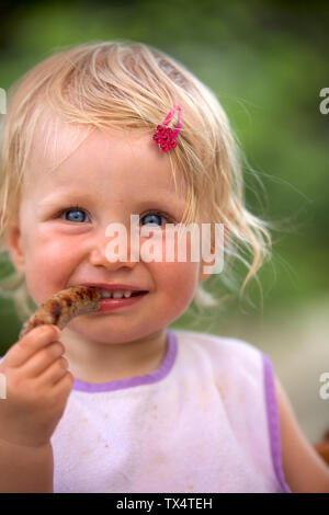 Portrait de petite fille blonde avec bib et haipin rose saucisse manger Banque D'Images