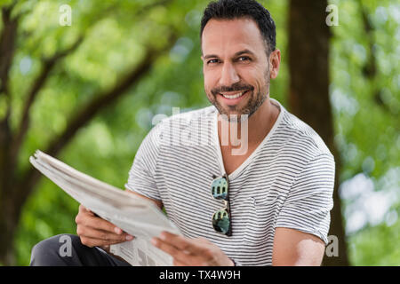 Portrait of smiling man reading newspaper in park Banque D'Images