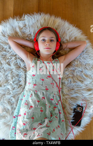 Girl lying on carpet à écouter de la musique avec des écouteurs et smartphone Banque D'Images