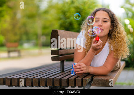 Jeune femme couché sur banc, soufflant des bulles de savon Banque D'Images