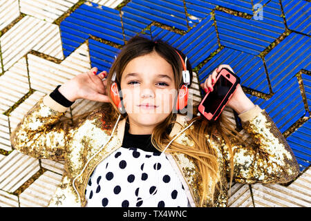 Portrait of Girl wearing golden sequin jacket à l'écoute de la musique avec des écouteurs et smartphone Banque D'Images