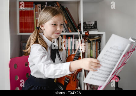 Smiling girl avec violon en regardant les notes sur le support musical Banque D'Images