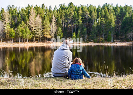 France, Pyrénées, vue arrière de père et fille assis côte à côte devant un lac Banque D'Images