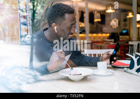 Smiling Young man with earphones et smartphone derrière la vitre dans un restaurant Banque D'Images