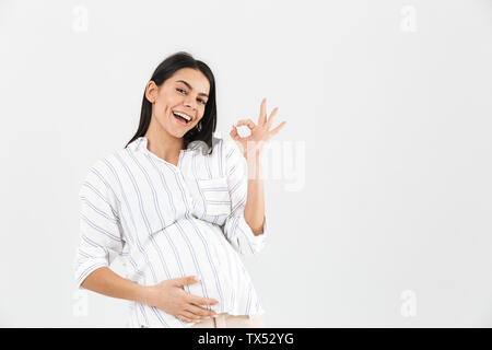 Photo de happy pregnant woman 30s avec gros ventre en souriant et montrant ok sign isolated over white background Banque D'Images