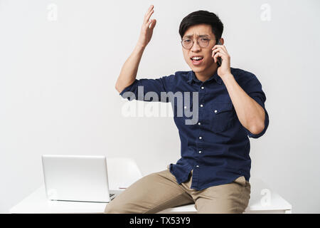 Photo de l'Asie a souligné businessman talking on smartphone pendant le travail avec laptop in office Banque D'Images