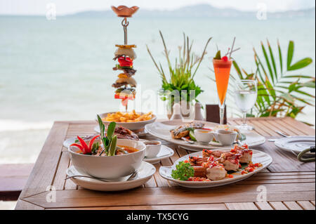 Variété d'aliments, des côtes de porc rôti, steak de boeuf, fruits de mer et soupe épicée sur table à manger en mer tropicale Banque D'Images