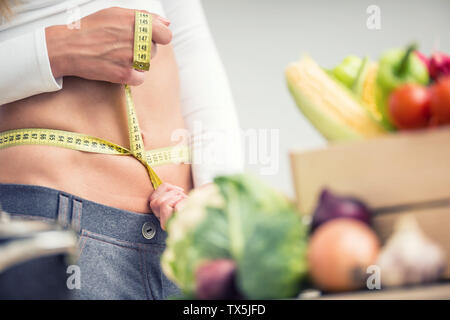 Femme taille avec un ruban à mesurer plus de boîte en bois avec des légumes. Banque D'Images