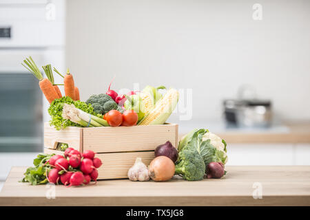 Boîte en bois plein de légumes frais sain. Brocoli à l'ail oignon radis le maïs en table de cuisine en bois. Banque D'Images