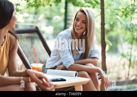 Deux jeunes filles gaies assis au café en plein air, de boire des smoothies Banque D'Images