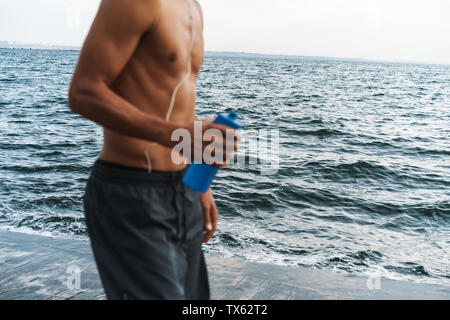 Portrait d'un fort beau jeune homme sportif africain en plein air sur la plage mer holing bouteille avec l'eau. Banque D'Images