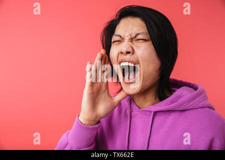 Gros plan Photo de angry asian guy 20s port sweatshirt crier tout en étant isolé sur fond rouge furieux Banque D'Images