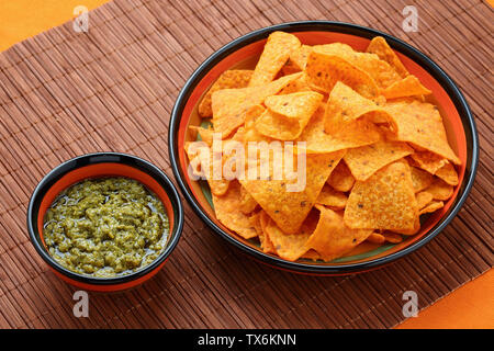 Portrait de sauce pesto au basilic avec des nachos croustilles de maïs dans de pimpantes assiettes sur un tapis de table en bambou Banque D'Images