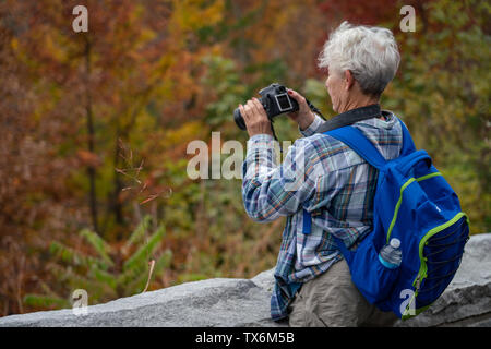 Une femme plus âgée avec un sac à dos sur prend des photos de la montagne en automne. Banque D'Images