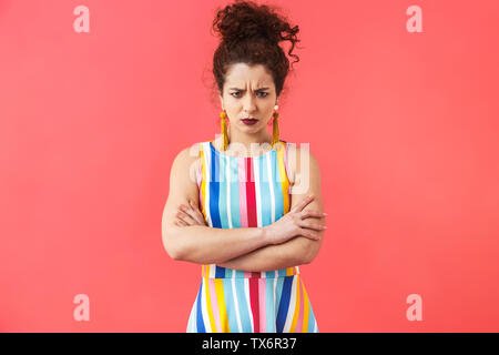 Portrait d'une jolie femme en colère portant robe rayée isolés sur fond rose, les bras croisés Banque D'Images