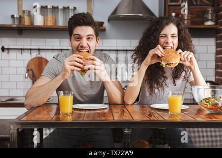 Cheerful couple heureux de manger des hamburgers à la cuisine Banque D'Images