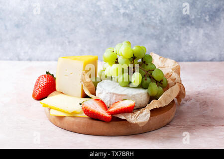 Différents fromages avec fraises et raisins sur une planche en bois libre Banque D'Images