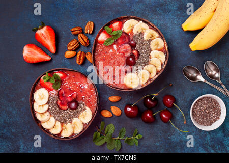 Petit-déjeuner sain. Bol smoothie aux fraises, cerises, amandes et noix, noix sur une base de béton bleu. Vue de dessus. Banque D'Images