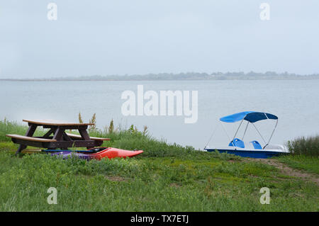 Kayak et bateau échoué sur Grassy Lake Shore près de table de pique-nique au cours de la tempête de pluie au lac Banque D'Images