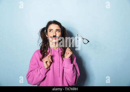 Portrait of happy princess girl holding paper fake moustache et lunettes de stick isolé sur fond bleu en studio Banque D'Images