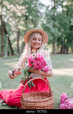 Fleuriste femme romantique en fait un chapeau de paille avec bouquet de fleurs de pivoines rose piscine Banque D'Images