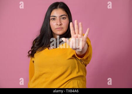 Femme faisant le geste d'arrêt tout en courbes, avec de graves et d'expression de colère sur fond rose- Latina woman Banque D'Images