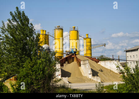 Photo industrielle avec des tas de gravier et sable dans la cimenterie avec trois gros silo jaune. Fosse de béton pour le ballast dans l'usine de ciment. Banque D'Images