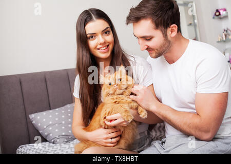 Beau jeune couple sur le lit en train de jouer avec un chat rouge Banque D'Images