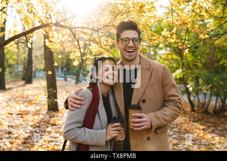 Portrait of laughing couple homme et femme à boire le café à emporter de tasses de papier tout en marchant dans le parc en automne Banque D'Images