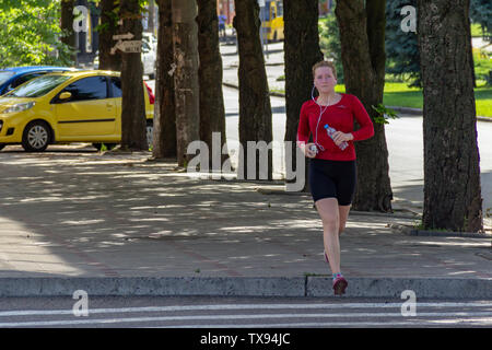 Dniepr, l'UKRAINE - 16 juin 2019 : Jeune fille va pour le sport sur rue. Jogging de bien-être. Femme en rouge T-shirt et chaussures de sport noir tourne-al Banque D'Images