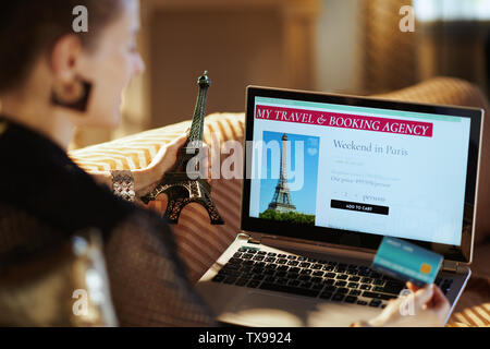Au cours de l'épaule en blouse noire femme au foyer moderne avec carte de crédit ou de la tour Eiffel à la recherche de chambre d'hôtel sur le site web de réservation en ligne assis sur Banque D'Images