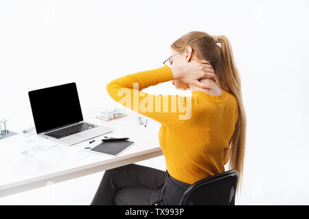 Vue latérale d'une belle jeune femme fatiguée graphic designer assis sur le lieu de travail travaillant sur écran blanc ordinateur portable et tablette sur isolés Banque D'Images