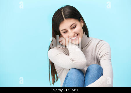 Studio portrait d'une jolie femme de race blanche, assis sur le plancher, à la recherche vers le bas smiling, isolé sur fond bleu Banque D'Images