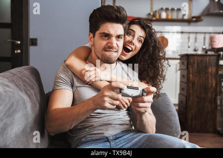 L'image de couple homme et femme 30s assis sur un canapé à la maison et jouer à des jeux vidéo avec une manette Banque D'Images