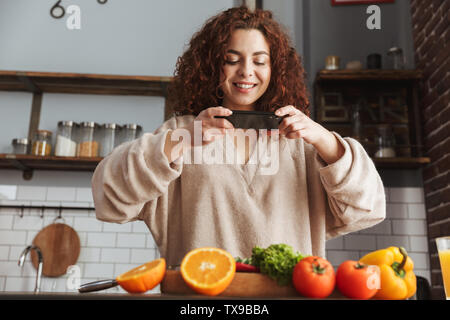 Image de beau caucasian woman taking photo de nourriture sur smartphone pendant la cuisson des légumes frais en salade cuisine intérieur à la maison Banque D'Images