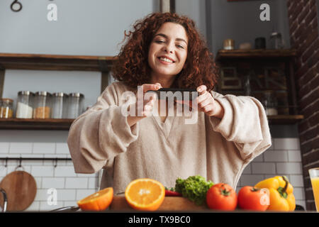 Image de jolie caucasian woman taking photo de nourriture sur smartphone pendant la cuisson des légumes frais en salade cuisine intérieur à la maison Banque D'Images