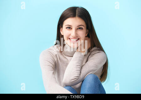 Studio portrait d'une jolie femme de race blanche, assis sur le plancher, smiling, isolé sur fond bleu Banque D'Images