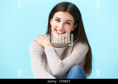 Studio portrait d'une jolie femme de race blanche, assis sur le plancher, smiling, isolé sur fond bleu Banque D'Images