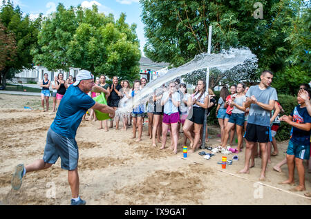 Odesa rgn. L'Ukraine, le 7 août 2018 : Le gars verse de l'eau à partir d'un seau sur la foule d'adolescents avant les sports d'eau de la concurrence dans le camp d'été Banque D'Images