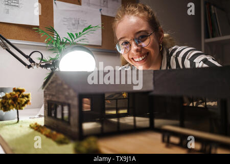 Photo de femme professionnelle laughing architect wearing glasses la conception de projet avec maison modèle et assis à vert au travail Banque D'Images