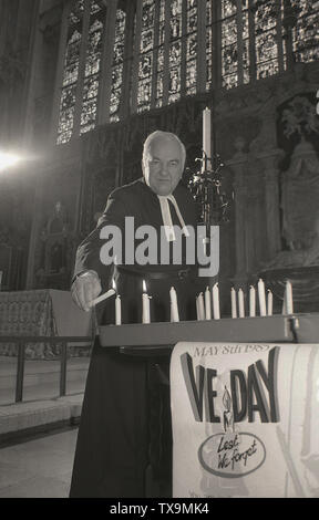 Mai 1985, ..Nous nous souviendrons.....un prêtre bougies d'éclairage dans une église en souvenir de ceux qui sont morts dans la DEUXIÈME GUERRE MONDIALE et de célébrer 40 ans de la journée de la guerre en Europe est terminée, connu comme le jour de la Victoire en Europe (), Angleterre, Royaume-Uni. Banque D'Images